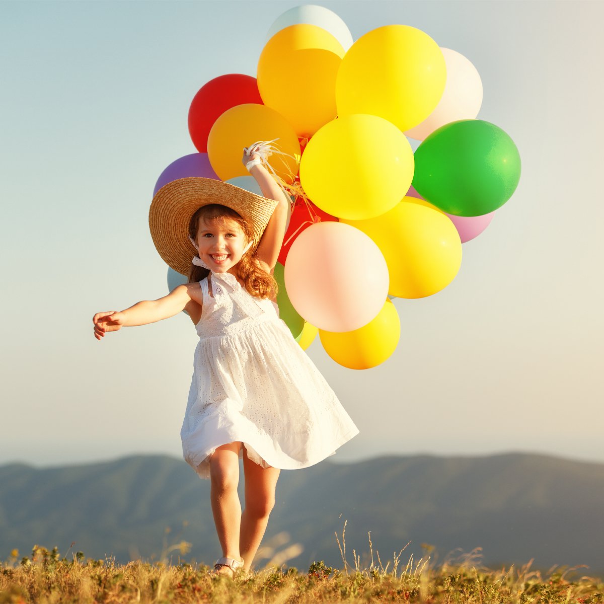 Girl with colourful balloons on mountain meadow